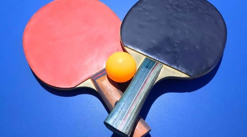 Zwei Tischtennisschläger und ein Tischtennisball auf einer blauen Tischtennisplatte