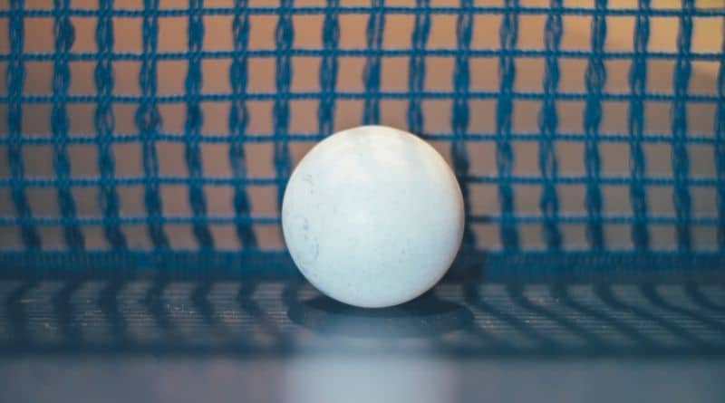 Ein weißer Tischtennisball vor einem blauen Netz