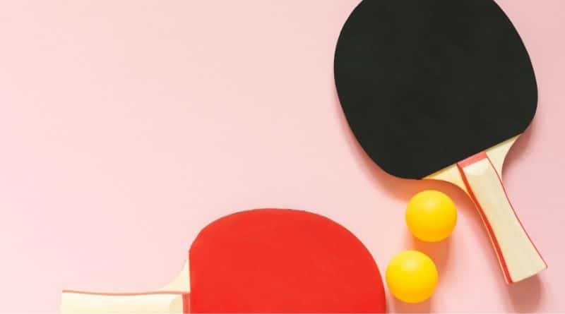 Zwei Tischtennisschläger und 2 orangene Bälle liegen auf einer rosa Fläche