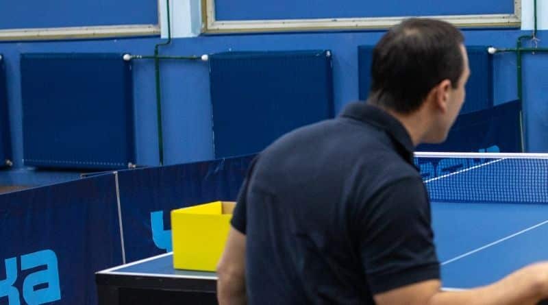 Blaue Tischtennisplatten Umrandungen stehen um einer Tischtennisplatte, an der ein Mann spielt