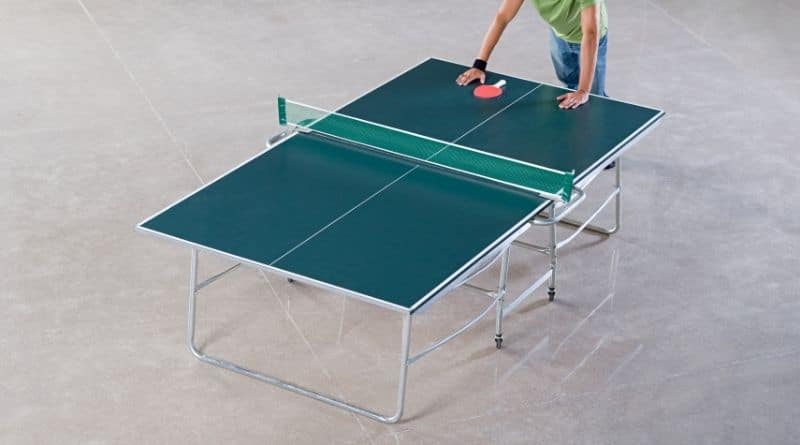 Tischtennisspieler stützt sich mit beiden Händen auf einer grünen Tischtennisplatte ab