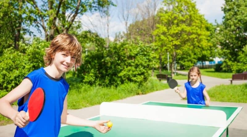 Zwei Kinder spielen draußen an einer kleinen Tischtennisplatte