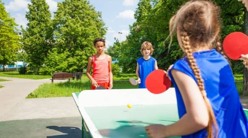 Kinder spielen draußen an einer Tischtennisplatte